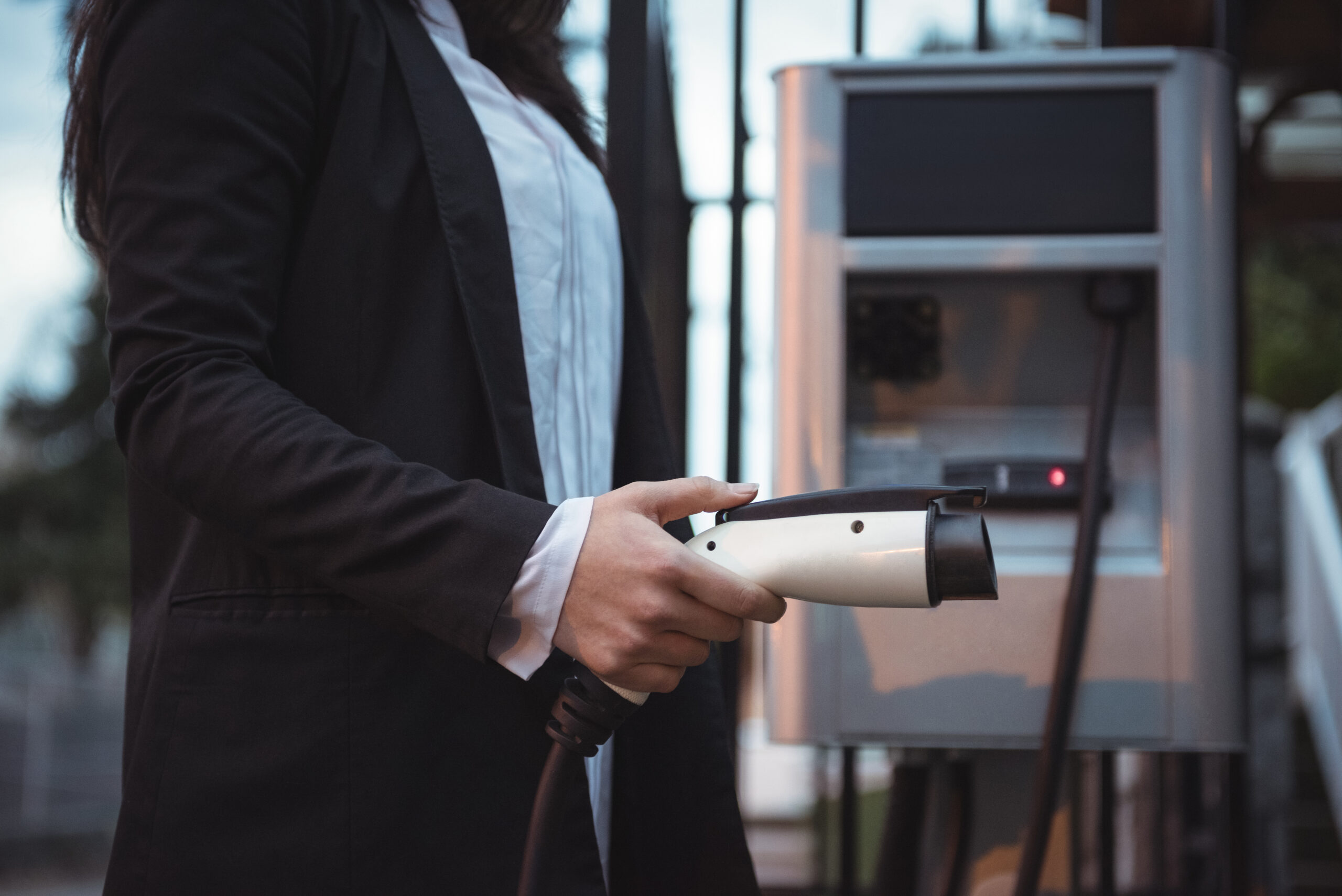 Mid section of woman holding car charger at electric vehicle charging station